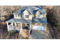 Two-story house with wraparound porch and attached garage, nestled in a wooded area at 5240 Indigo Moon Way, Raleigh, NC 27613