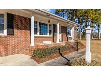 Charming brick home featuring a welcoming front porch with classic white columns and manicured landscaping at 205 N Augusta Ave, Benson, NC 27504