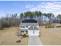 Aerial view of a two-story house with solar panels, a driveway, and a wooded backdrop at 70 Kinsale Ct, Fuquay Varina, NC 27526