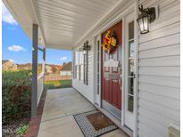 Inviting front porch with autumn decor, a red door, and sidelights welcomes visitors at 102 Redstone Dr, Gibsonville, NC 27249