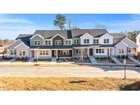 New construction townhomes with modern farmhouse style exteriors, paved sidewalks and young trees under a clear blue sky at 3935 Willow Gate Way, Knightdale, NC 27604