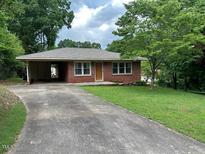 Cozy single-story brick home featuring an attached carport and a well-maintained front yard with mature trees at 404 W Ninth St, Siler City, NC 27344