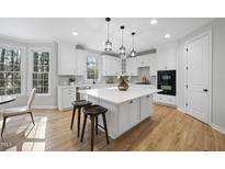 Bright kitchen boasts white cabinets, a spacious island with seating, pendant lighting, and stainless steel appliances at 109 Aspenridge Dr, Holly Springs, NC 27540
