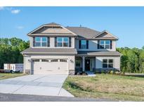Two-story house with beige siding, gray stone accents, and a three-car garage at 45 River Chapel Dr, Fuquay Varina, NC 27526