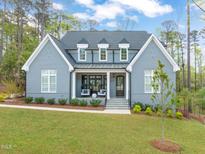 Beautiful two-story home with a gray brick facade, white trim, and a welcoming front porch with seating at 2721 Sanctuary Woods Ln, Raleigh, NC 27606