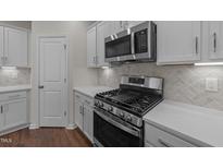 Modern kitchen featuring stainless steel appliances, white cabinets, stone countertops, and wood floors at 48 Railcar Way, Clayton, NC 27520