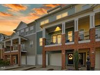 Beautiful townhome exterior showcasing brick accents, covered balconies and garage at sunset at 219 Broadgait Brae Rd, Cary, NC 27519