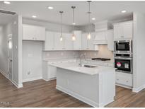 Modern kitchen features white cabinets, stainless steel appliances, and a large island with pendant lighting at 3854 Well Fleet Drive, Fuquay Varina, NC 27526