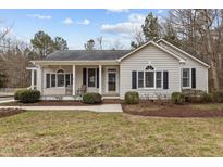 Beige house with a covered porch, landscaping, and a spacious lawn at 207 Meadowbrook Ln, Oxford, NC 27565