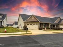 Charming home featuring a stone facade, two-car garage, and well-maintained landscaping under a dramatic sky at 3947 Foxglove Trl, Burlington, NC 27215