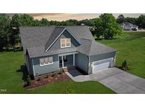 Beautifully landscaped, the charming home features a gray roof, an attached garage, and light green siding at 83 Nottoway Lane, Wendell, NC 27591