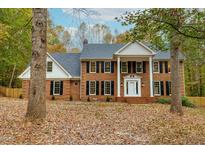 Stately brick home featuring a columned entrance and mature trees in a lush, leafy front yard at 11705 Appaloosa E, Raleigh, NC 27613