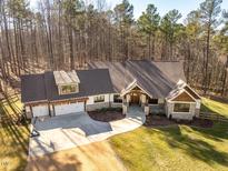 An aerial view of a spacious home showcasing a three-car garage, stone accents, and an expansive wooded lot at 2918 Borland Rd, Hillsborough, NC 27278
