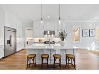 Bright kitchen features white cabinets, an island with seating, stainless steel appliances, and hardwood floors at 7212 Summer Tanager Trl, Raleigh, NC 27614