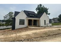 Newly built home with a white painted brick facade, dark roof, and wood porch posts, creating a modern farmhouse appeal at 395 Meadow Walk Dr, Fuquay Varina, NC 27526