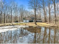 View of the home from across the pond, with a two-car garage and mature trees. Reflection on the water at 4051 Silk Hope Gum Springs Rd, Pittsboro, NC 27312