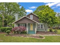 Charming home featuring a stone chimney, landscaped yard, mature trees, and a inviting yellow front door at 209 E Winston St, Youngsville, NC 27596