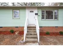 Inviting home with a brick foundation, painted pale green siding, and front door flanked by mulched landscaping at 809 S Plum St, Durham, NC 27701