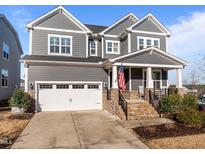 Charming two-story home with gray siding, stone accents, an American flag, and a two-car garage at 516 Ivy Arbor Way, Holly Springs, NC 27540