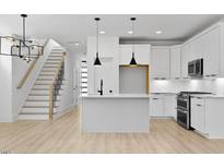 Bright kitchen with island, stainless appliances, white cabinets, and open staircase at 140 E End Ave # 2, Durham, NC 27703