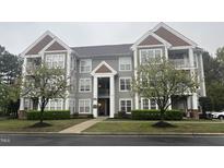 View of the gray home exterior showcasing mature trees, manicured lawns, and multiple window views at 1828 Parkside Village Dr, Clayton, NC 27520