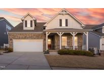 Charming two-story brick home with inviting front porch and well-manicured lawn at sunset at 117 Blue Hydrangea Ln, Holly Springs, NC 27540