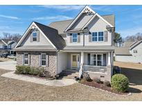 Charming two-story home featuring stone accents, gray siding, manicured landscaping, and a welcoming yellow front door at 109 Hammermill Dr, Fuquay Varina, NC 27526