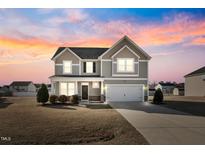 Charming two-story home featuring a two-car garage, neutral siding, and a well-manicured front yard at sunset at 109 Perignon Dr, Princeton, NC 27569