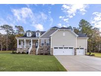 Beautiful home featuring a stone facade, a charming front porch, and a three-car garage on a well-manicured lawn at 409 Grading Stick Ct, Angier, NC 27501