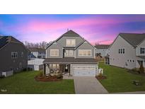 Charming two-story home featuring a welcoming front porch and a manicured lawn at dusk at 408 Faxton Way, Holly Springs, NC 27540