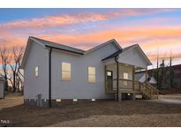 Charming home featuring light siding, a covered front porch, and manicured lawn, all under a colorful sunset sky at 608 Gilmer St, Burlington, NC 27217