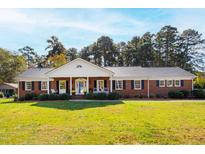 Charming brick home featuring a cozy front porch, mature landscaping, and classic architectural details at 4409 Driftwood Dr, Raleigh, NC 27606