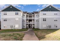 Three-story building with light gray siding, dark green trim, and balconies above entrance walkway at 2020 University Woods Rd # 203, Raleigh, NC 27603