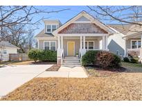 Charming home featuring a welcoming front porch, shingle detailing, a bright yellow front door, and manicured landscaping at 2715 Edmund St, Durham, NC 27705