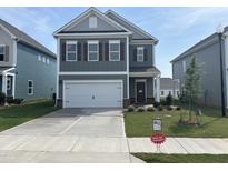 Two-story home featuring a gray exterior, white garage door, and manicured front yard with 'Must See Upgrades' sign at 52 Commons Cir, Clayton, NC 27520
