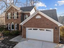 Two-story brick home with a two-car garage and mature landscaping under a partly cloudy sky at 118 N Drawbridge Ln, Cary, NC 27513