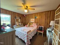 Cozy bedroom features wood paneling, ceiling fan, and bright natural light from a window at 322 Blackstone Rd, Sanford, NC 27330
