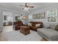 Spacious living room features a ceiling fan, tan leather furniture, decor, and large windows for natural light at 1104 Pebblestone Dr, Durham, NC 27703