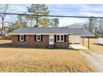 Charming brick home with black shutters and a convenient carport under a clear blue sky at 307 S Main St, Four Oaks, NC 27524