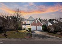 Charming two-story brick home featuring a well-manicured lawn and a two-car garage at sunset at 715 Southshore Pkwy, Durham, NC 27703