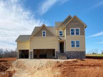 New two-story home showcasing a stone foundation, an attached two-car garage and yellow siding on a sunny day at 4875 Grosbeak Ct, Mebane, NC 27302