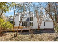 Charming home exterior with a wooden deck, white siding, and black window frames surrounded by lush greenery and trees at 7 Hampton Hill Pl, Chapel Hill, NC 27517