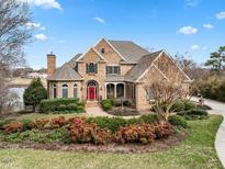 Charming two-story brick home featuring a manicured lawn, mature landscaping, and a welcoming red front door at 210 Lake Manor Rd, Chapel Hill, NC 27516