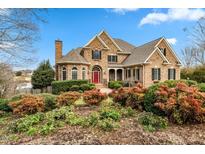 Charming two-story brick home featuring a manicured front yard with lush landscaping, and a bright red front door at 210 Lake Manor Rd, Chapel Hill, NC 27516