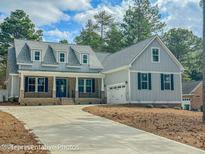 Charming two-story home featuring a well-manicured lawn, blue door, dormer windows, and an attached two car garage at 515 Sanctuary Trl, Cameron, NC 28326