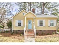 Charming yellow home featuring a brick foundation, blue door, white shutters and a landscaped front yard at 2618 Elgin St, Durham, NC 27704