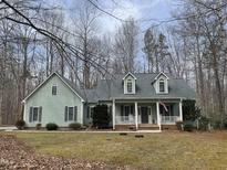 Charming light green home with a welcoming front porch and dormer windows surrounded by a wooded lot at 613 Hamecon Place, Cedar Grove, NC 27231