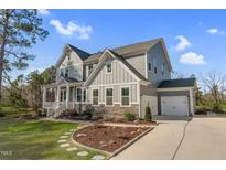 Charming gray two-story home boasts a manicured lawn, stone accents, and a three-car garage at 8424 Brady Pointe Rd, Fuquay Varina, NC 27526