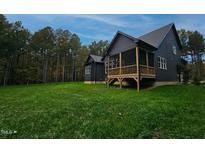 A charming dark-siding home with a wooden porch and stairs on a green lawn under a blue sky at 1147 Henderson Tanyard Rd, Pittsboro, NC 27312