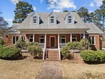 Charming brick home featuring a welcoming front porch, dormer windows, and professionally landscaped yard at 6336 Wrenwood Ave, Raleigh, NC 27607